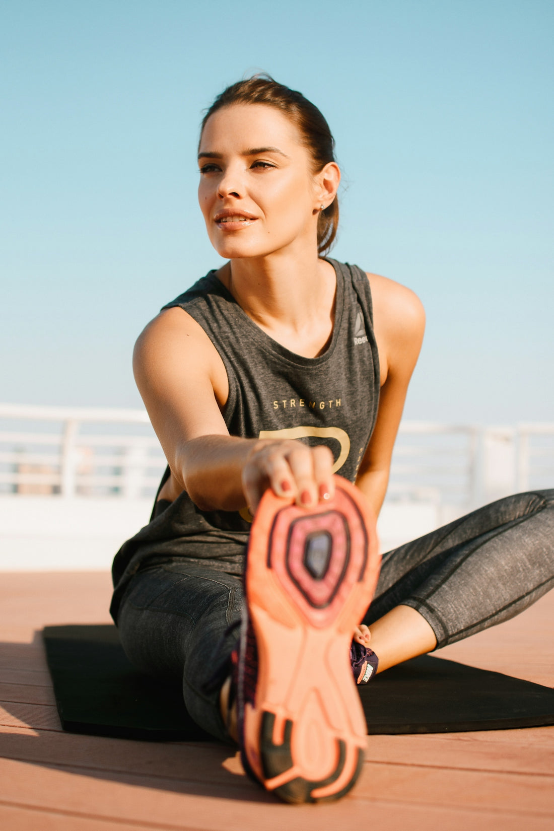 A woman in a grey tank top stretching her leg on a mat